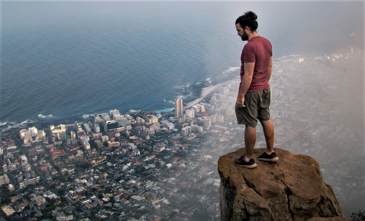 A man standing on a cliff, gazing down at the breathtaking view of Cape Town.